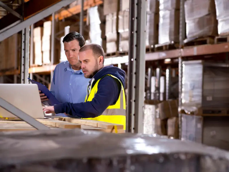 Two warehouse workers looking at a laptop in the warehouse.
