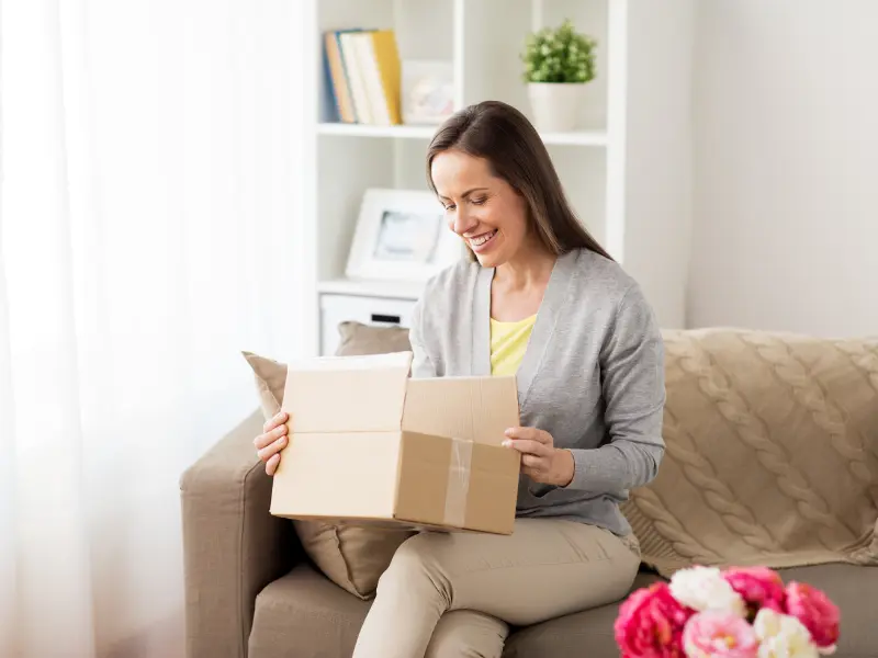 Woman opening a cardboard box package on a couch.